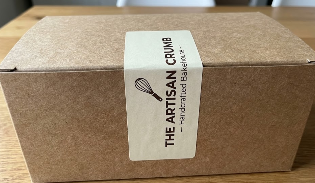 Rustic unbleached kraft cupcake box sealed with a custom-printed vertical brand sticker acting as a security label.