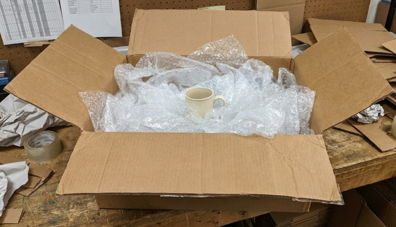Example of inefficient packaging: An oversized generic brown cardboard box overflowing with messy plastic bubble wrap surrounding a small ceramic mug, highlighting wasted space and 'air tax'.